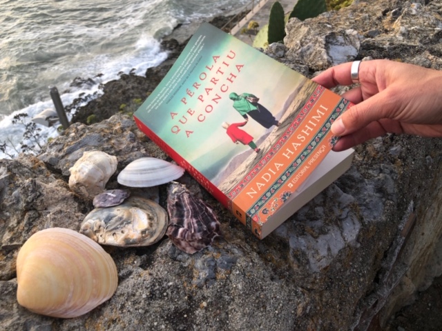 Livro «A pérola que partiu a concha» em fundo de conchas e mar