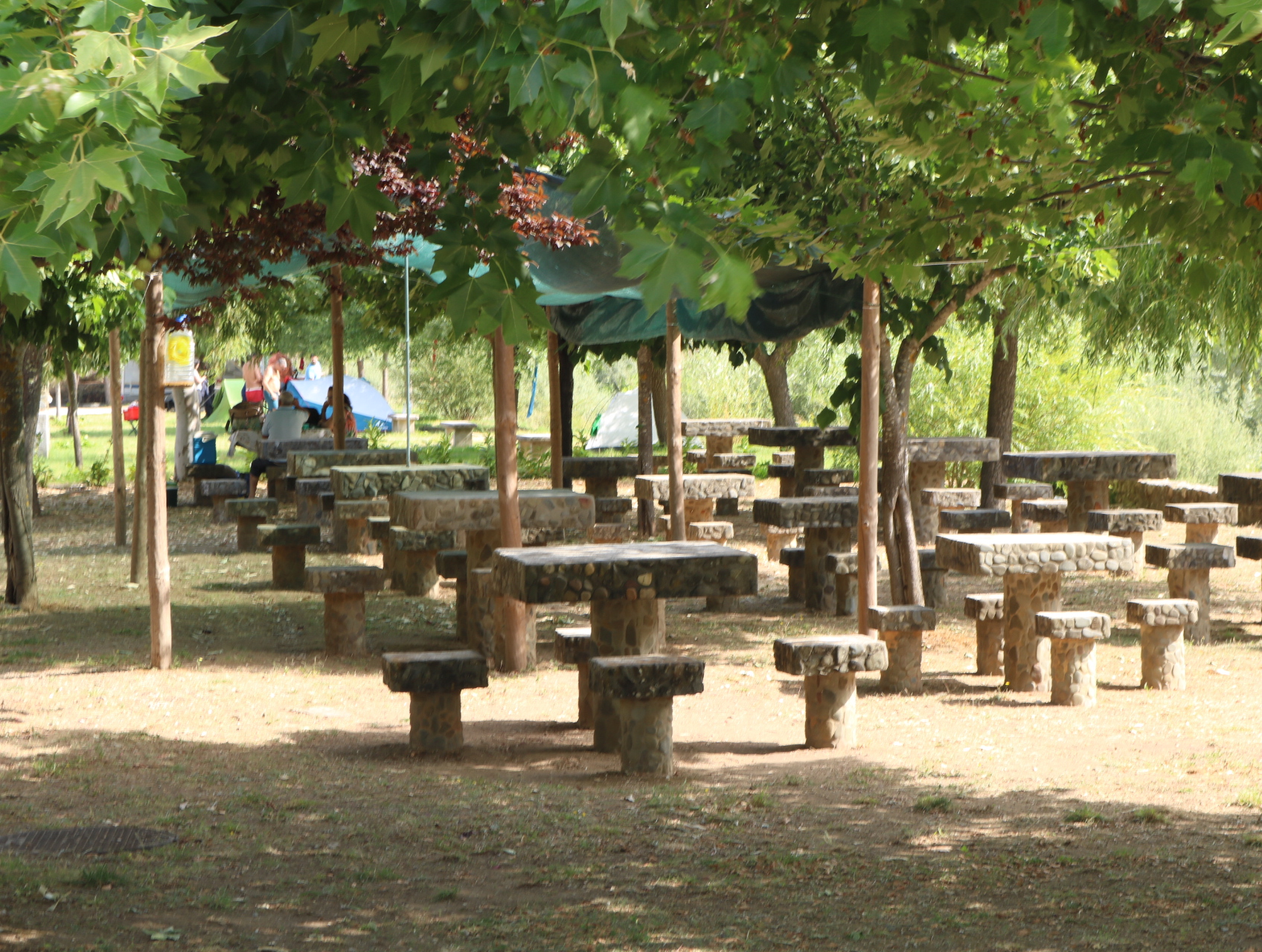 Mesas e bancos de pedra comuns à Praia Fluvial e ao Parque de Campismo de Bosteliim